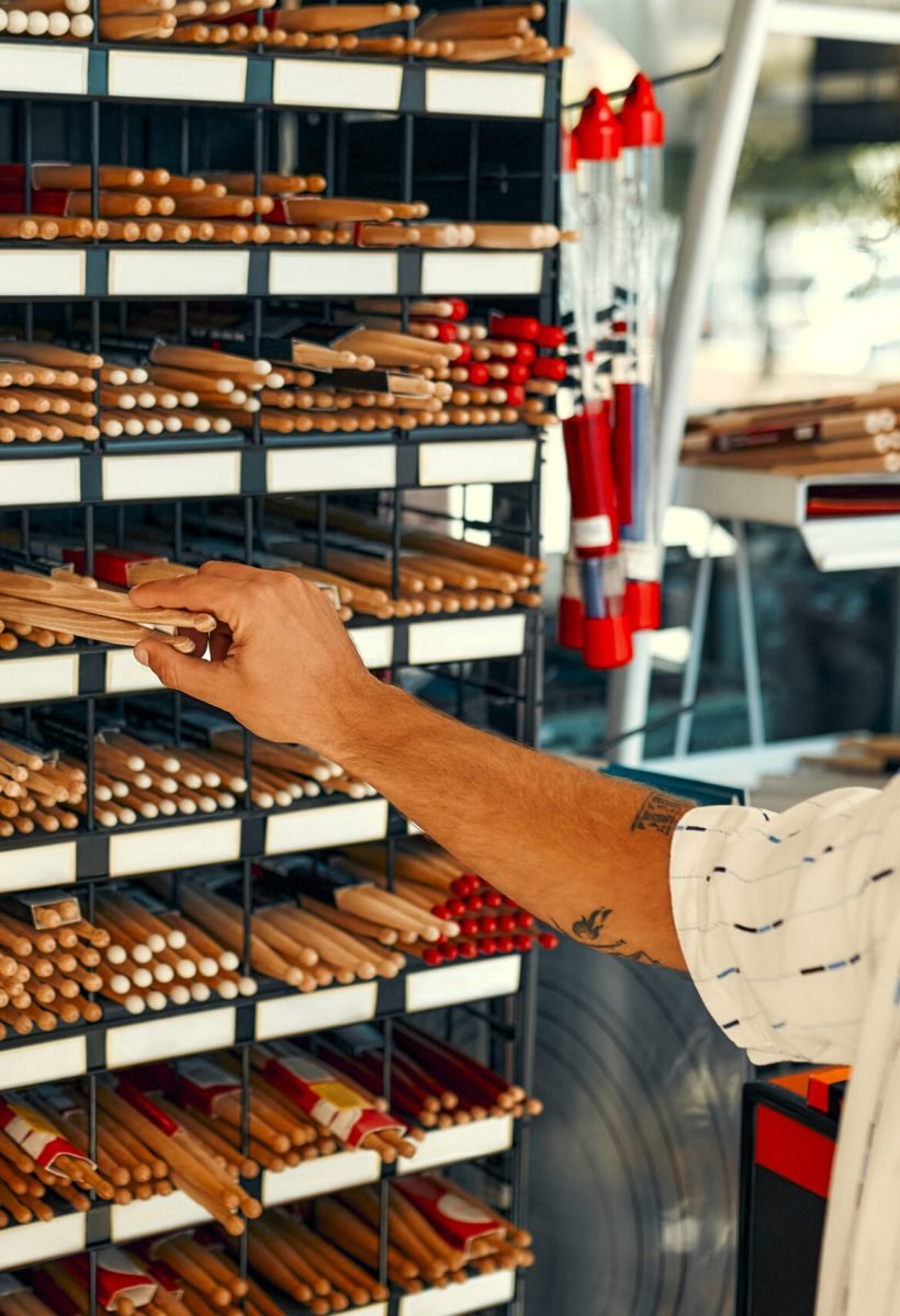 Handsome bearded curly man choosing a drum in a musical instrument store. Hobbies and recreation. A man buying drumsticks in a store. Shelves with many drumsticks.